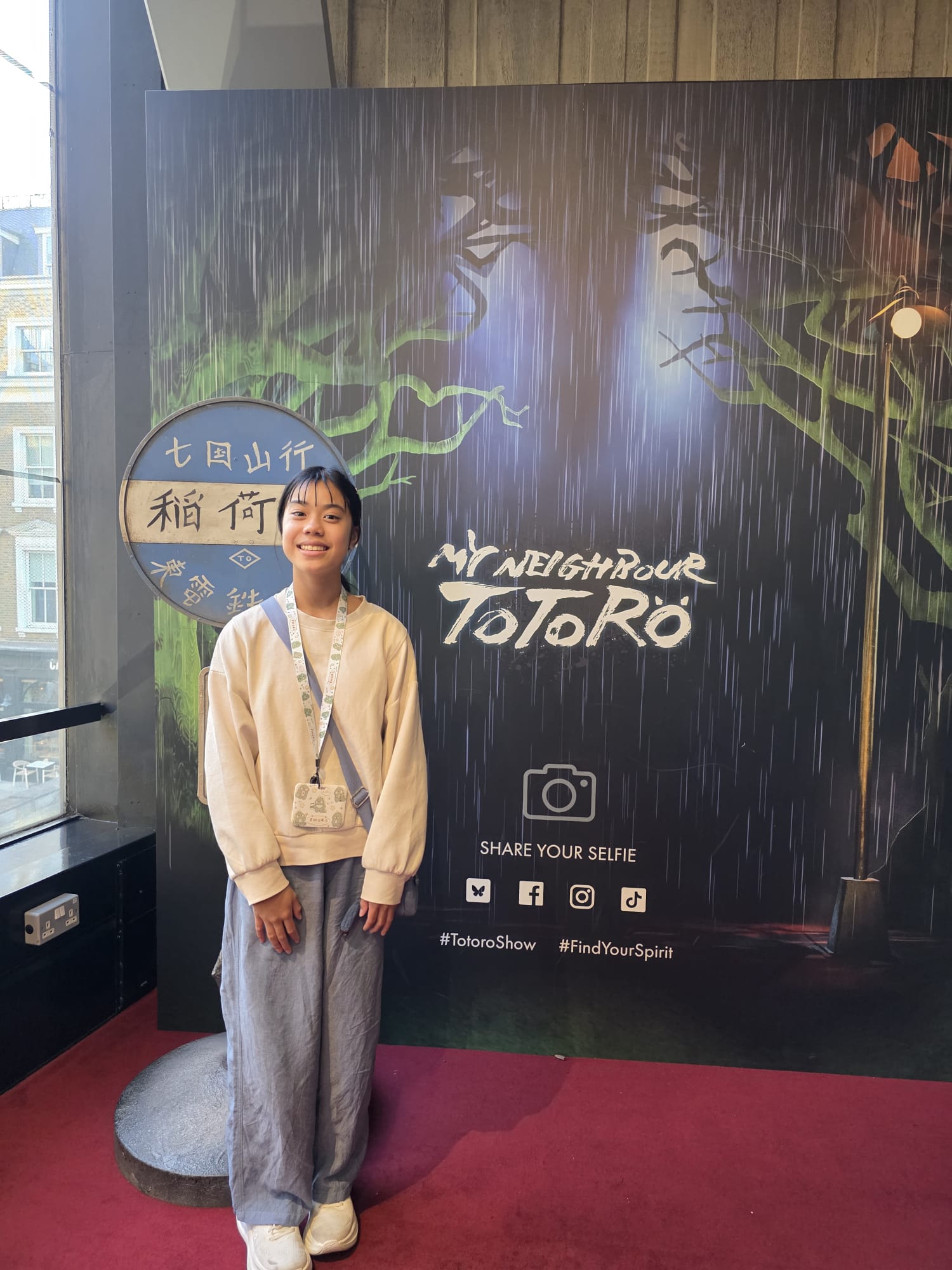 Photo of Cara standing next to the My Neighbour Totoro promotional stand at the Gillian Lynne Theatre